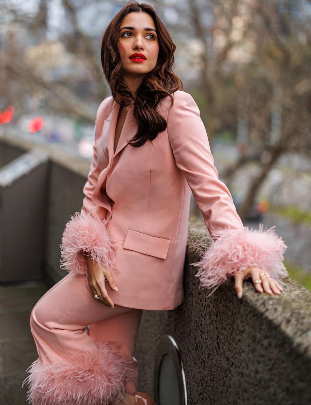 The beguiling beauty who always puts her best fashion forward sent shockwaves all over when she flaunted a chic blush pink pant suit in the streets of Melbourne. Her dreamy pantsuit which consisted a blush pink blazer and a matching pants was all about grace and elegance. The feather deatilings on the cuffs and hemline gave a glamorous vibe to her otherwise formal outfit. The 'Baahubali' star accessorised her dreamy outfit with beige pointed high heels, statement pearl gold rings and matching pearl drop earrings. With blushed cheeks, subtle eye shadow and centre-parted open hair-do, Tamannaah simply looked dazzling. The star looked ravishing as ever in her bold red lipstick.